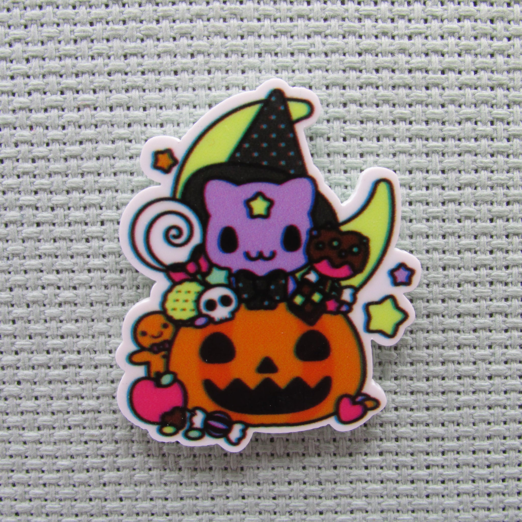 First view of the Purple Cat Wearing a Witch's Hat in a Carved Pumpkin full of Candy in Front of a Moon Needle Minder