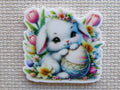 First view of Cute white bunny with an Easter Egg sitting in flowers minder.