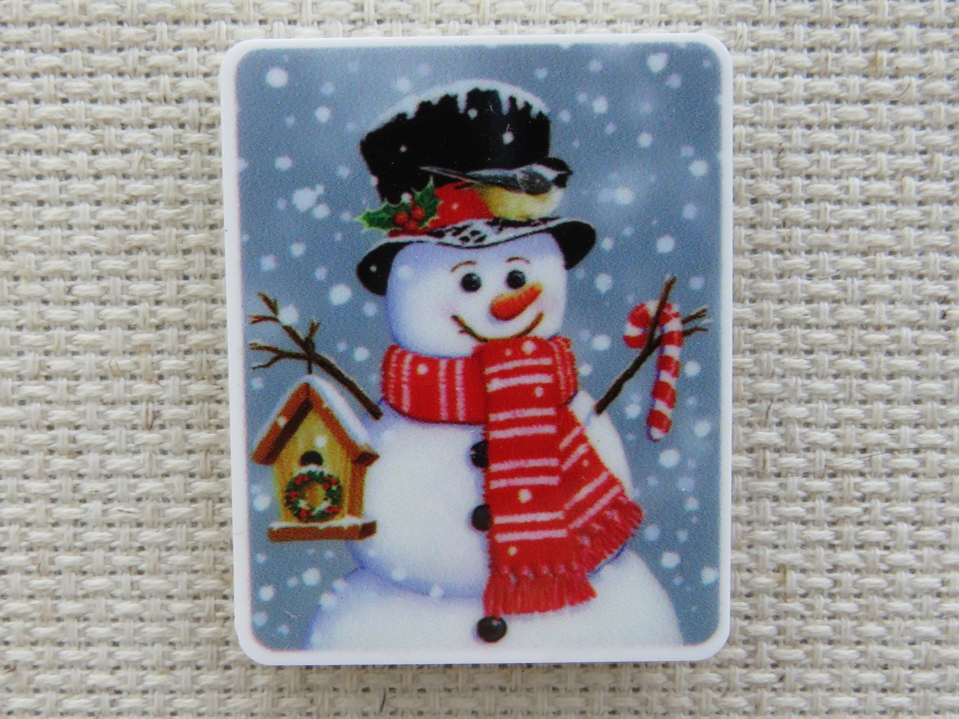 First view of Red scarf wearing snowman with a birdhouse in one hand and a candy cane in the other minder.